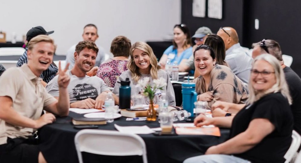 A smiling group of adults gathered around a table at a church class