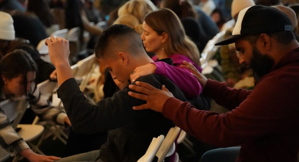 Church members praying over a young man, hands on his shoulders