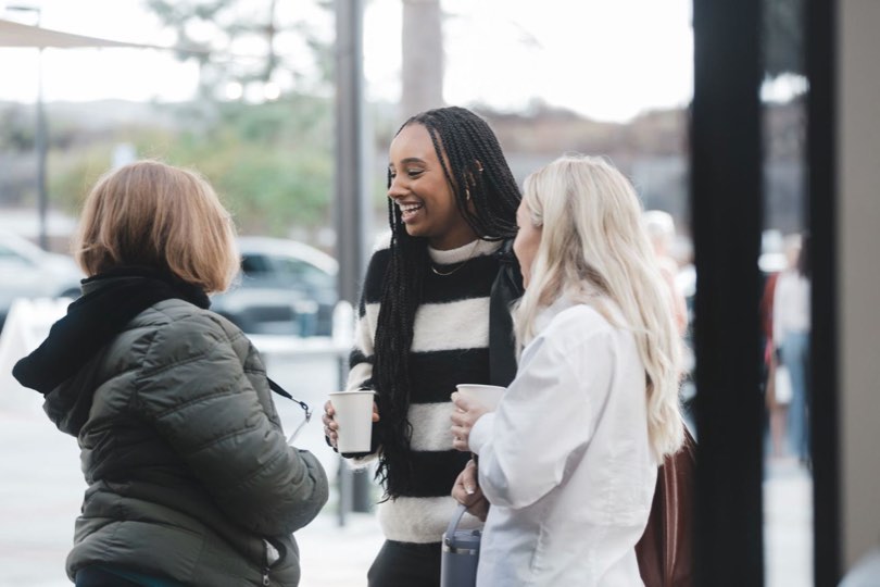 Three women chatting and laughing over coffee outside church